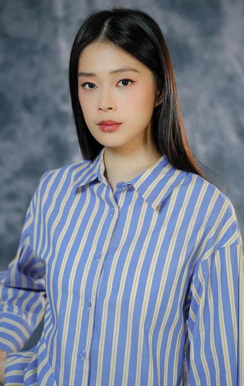 Atasan kemeja lengan panjang wanita Giselda warna biru klasik dengan motif garis-garis kuning, dilengkapi kerah rapi dan kancing depan penuh.