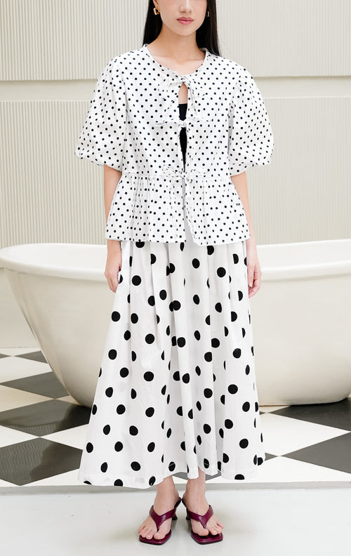 Baju atasan wanita Giselle Top warna putih motif polkadot hitam dengan detail tali ikatan depan (tie-front), lengan balon puff sleeve, dan potongan peplum mekar.