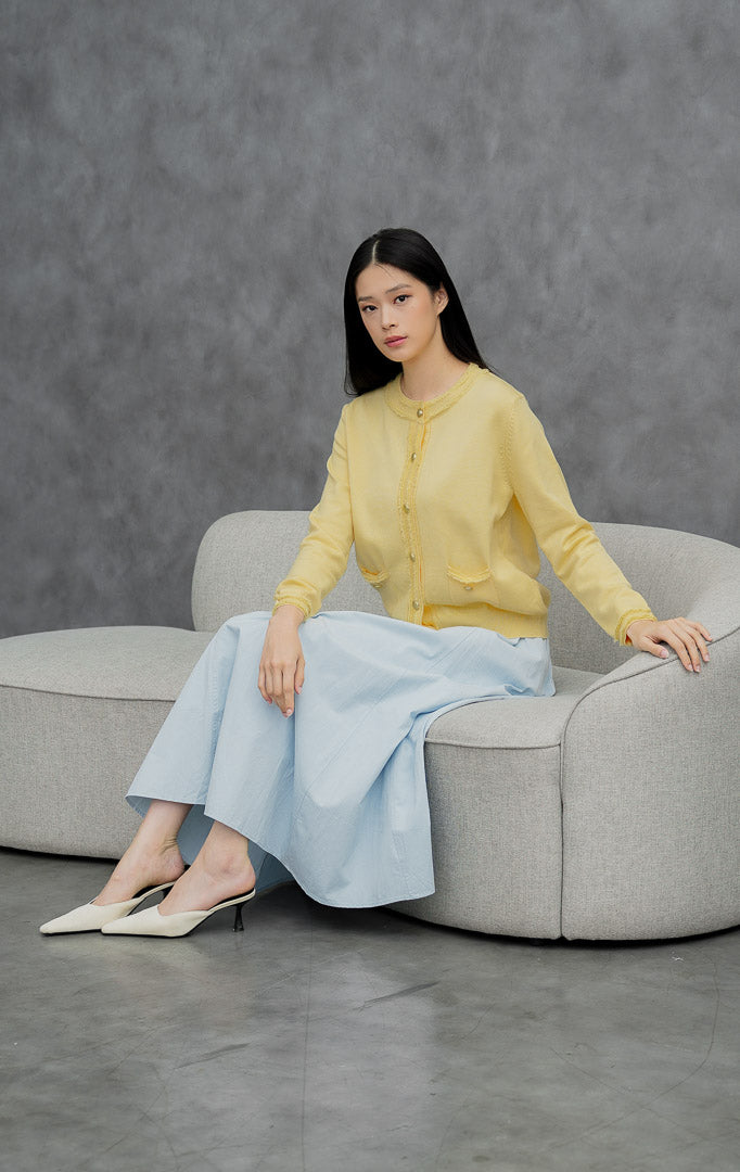 Kardigan rajut wanita lengan panjang warna kuning muda (butter yellow) Guilin Cardigan dengan detail rumbai (fringe trims), saku depan fungsional, dan kancing emas.