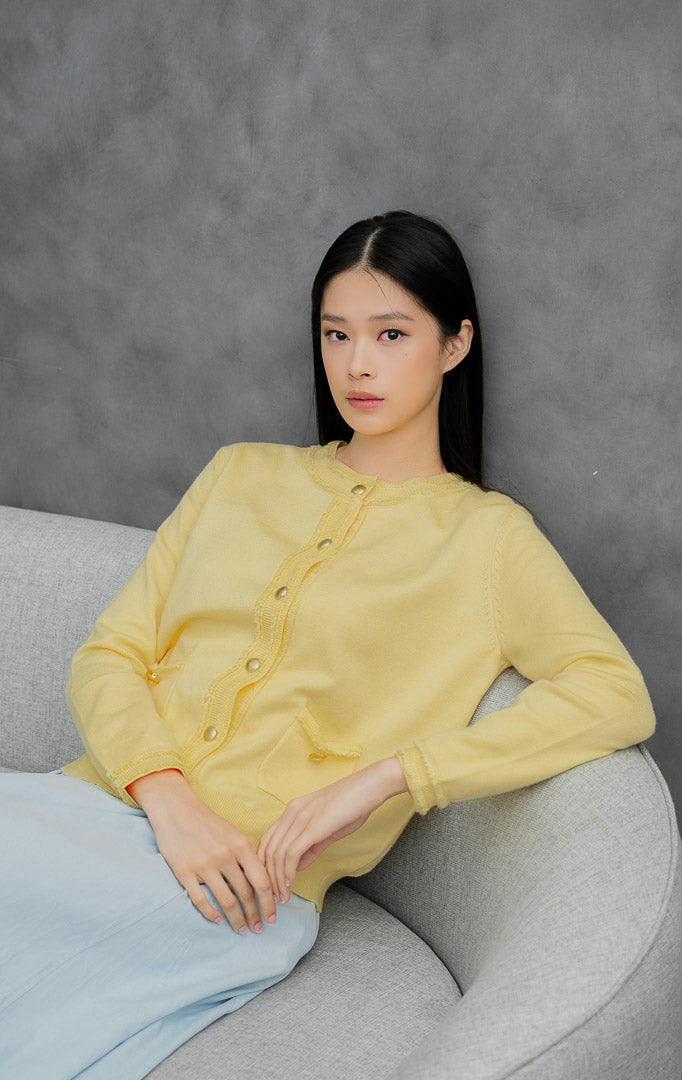 Kardigan rajut wanita lengan panjang warna kuning muda (butter yellow) Guilin Cardigan dengan detail rumbai (fringe trims), saku depan fungsional, dan kancing emas.