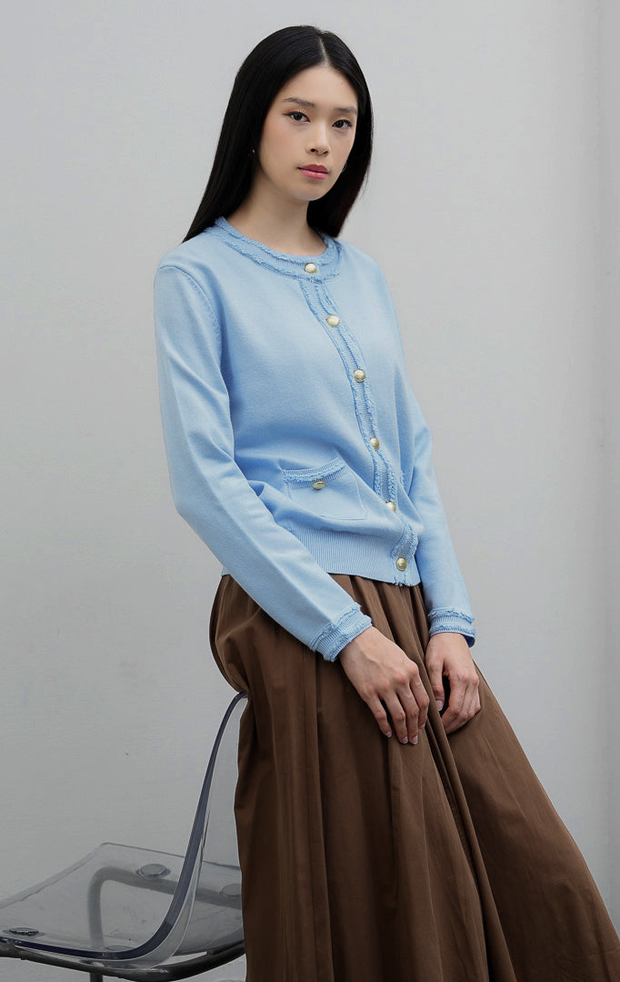 Kardigan rajut wanita lengan panjang warna biru muda (light blue) Guilin Cardigan dengan detail rumbai (fringe trims), saku depan fungsional, dan kancing emas.