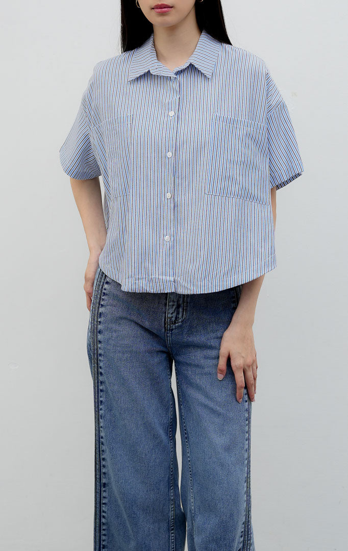 Kemeja katun wanita lengan pendek potongan boxy warna biru (blue) Hampton Top berkerah (spread collar) dengan motif garis vertikal (striped pattern), kancing depan, dan saku dada.