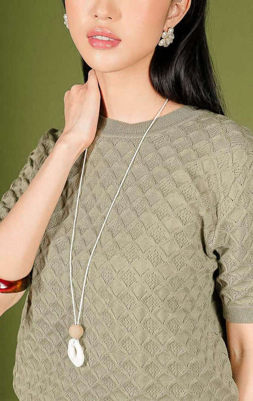 Atasan rajut wanita Harper Top warna olive (hijau zaitun) lengan pendek, dilengkapi kerah bulat (crew neck) beraksen rib, serta dihiasi motif rajutan bertekstur bentuk diamond atau wajik di seluruh permukaannya.