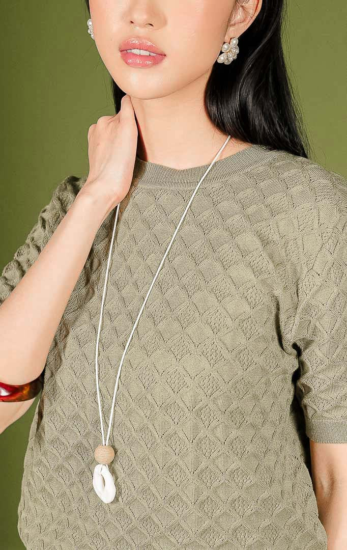 Atasan rajut wanita Harper Top warna olive (hijau zaitun) lengan pendek, dilengkapi kerah bulat (crew neck) beraksen rib, serta dihiasi motif rajutan bertekstur bentuk diamond atau wajik di seluruh permukaannya.
