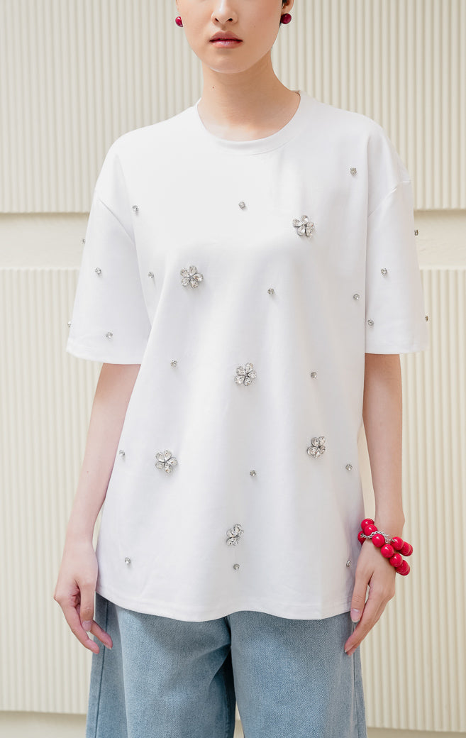 Kaos oversized wanita warna putih Haru Top dengan detail hiasan kristal floral rhinestone, kerah bulat, dan model santai bergaya streetwear.
