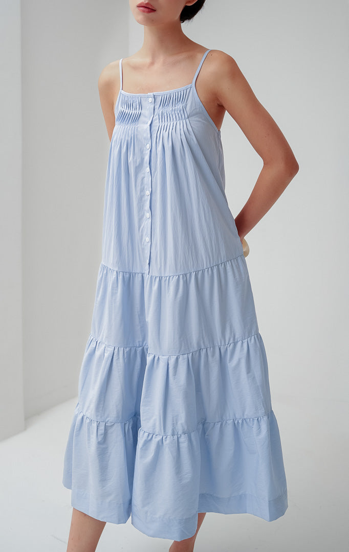 Maxi dress panjang wanita warna biru muda (light blue) Hathaway Dress berbahan katun dengan detail smocked yoke di dada, tali spageti (adjustable straps), dan gaun berundak (tiered silhouette).