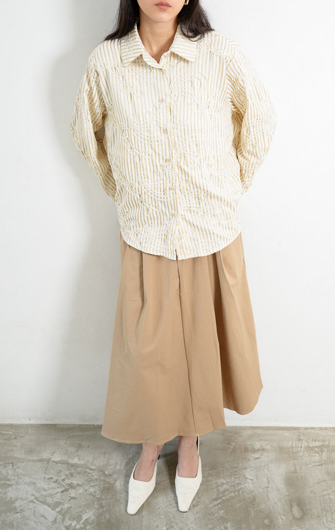 Kemeja wanita lengan panjang warna khaki Hawthorne Top berbahan tekstur motif garis dengan detail bordir timbul abstrak (intricate looped embroidery), kerah lebar (oversized collar), bukaan kancing depan, dan kelim melengkung (curved hem). 

