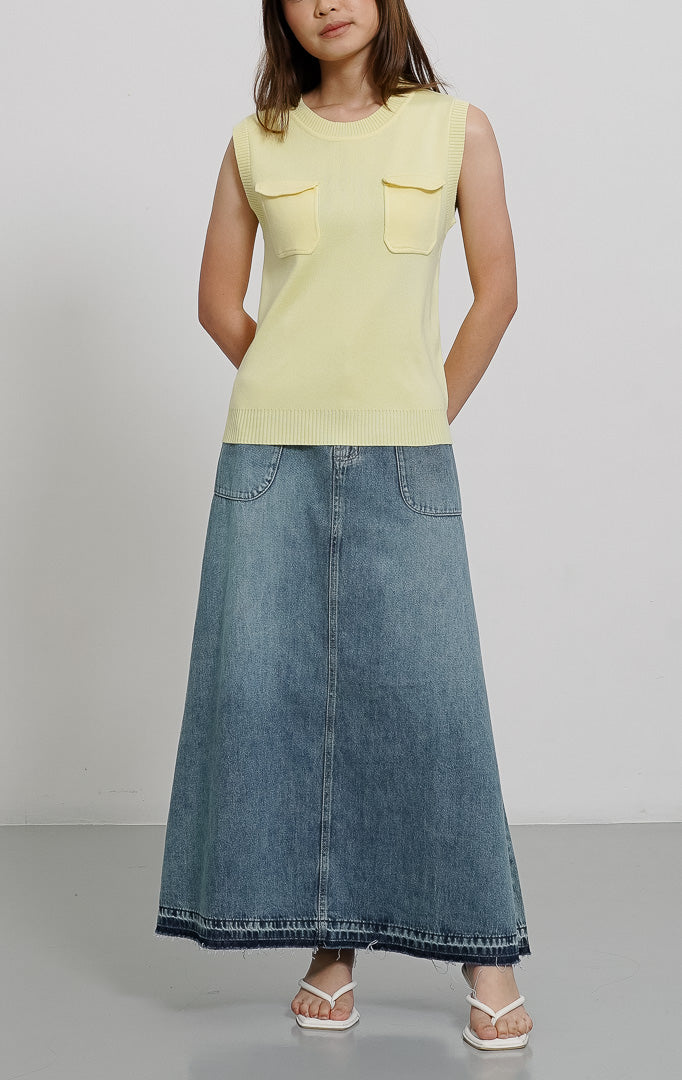 Model wanita mengenakan Heidi Top Yellow, atasan rompi rajut tanpa lengan warna kuning pastel dengan dua saku dada, dipadukan dengan rok denim panjang.