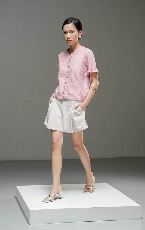 Outer rajut pendek wanita Henley Outer warna pink lengan pendek dengan tekstur motif, kancing depan warna emas, dua saku depan, dan detail ruffle hem. 