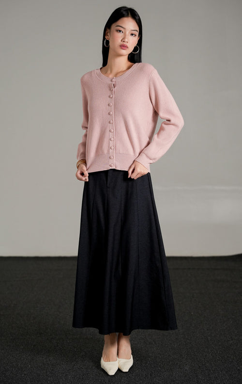 Hermione Knit Cardigan lengan panjang berwarna dusty pink dengan kancing depan tertutup, dipadukan dengan rok midi A-line hitam dan sepatu heels putih.