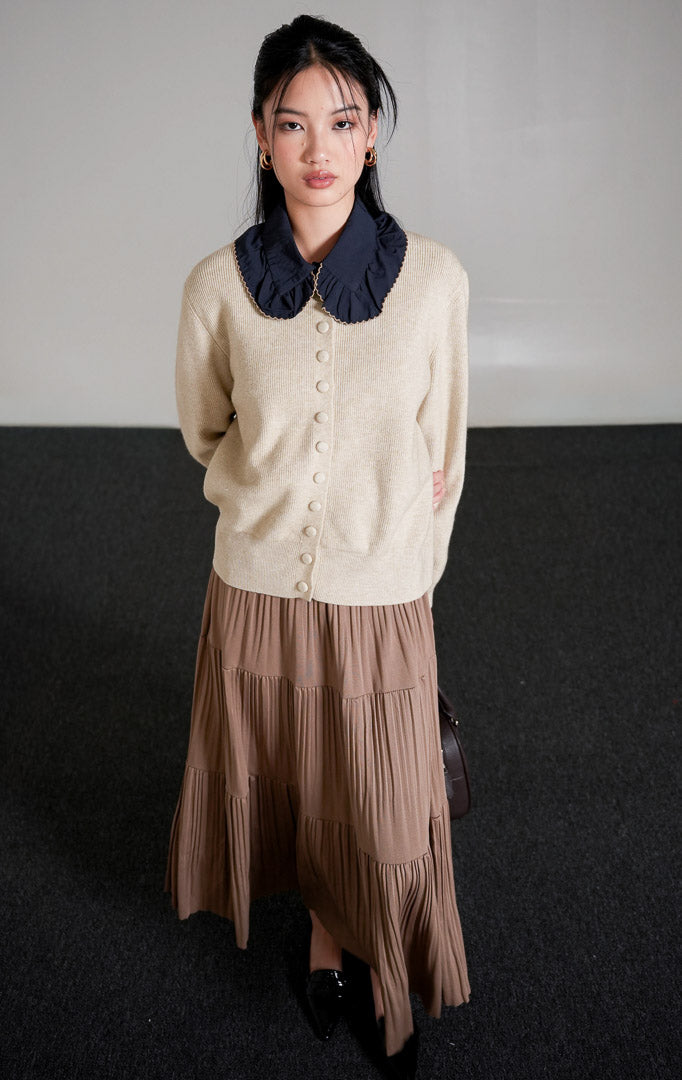 Hermione Knit Cardigan lengan panjang berwarna ivory (gading) dengan kancing depan tertutup, dipadukan dengan celana panjang bahan warna cokelat dan sepatu heels putih.

