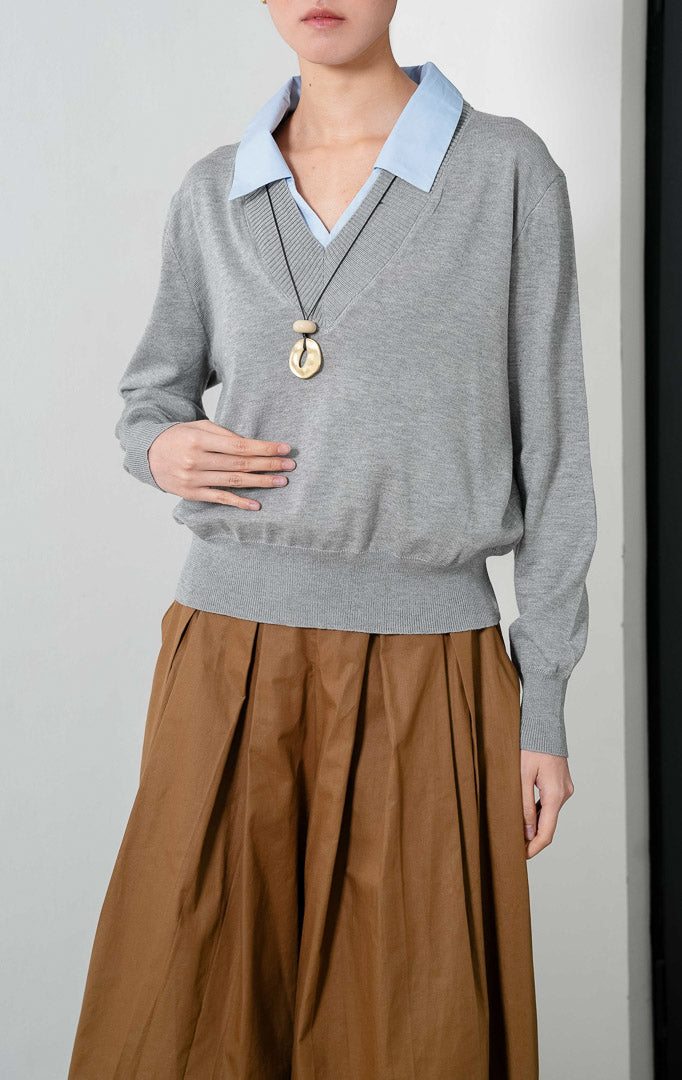 Sweater rajut lengan panjang warna abu-abu (grey knit sweater) Herra Sweater dengan kerah V (V-neck) dan detail aksen kerah kemeja warna biru di bagian dalam yang memberikan tampilan berlapis (contrasting blue collar layered appearance).