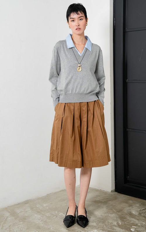 Sweater rajut lengan panjang warna abu-abu (grey knit sweater) Herra Sweater dengan kerah V (V-neck) dan detail aksen kerah kemeja warna biru di bagian dalam yang memberikan tampilan berlapis (contrasting blue collar layered appearance).
