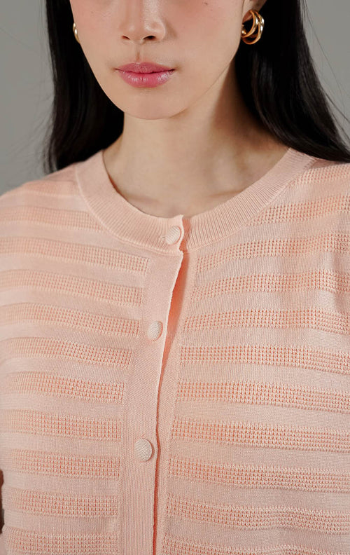 Annalina Cardigan Pink Peach dari This Is April, atasan rajut lengan pendek warna peach dengan motif garis benang timbul dan kancing depan.