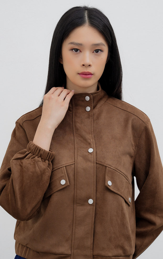 Jaket wanita warna cokelat tua (dark brown) Honoria Jacket berbahan campuran crinkled cotton-nylon dengan kerah tinggi (high-neck), bukaan kancing jepret (snap-button closure), dan saku fungsional.