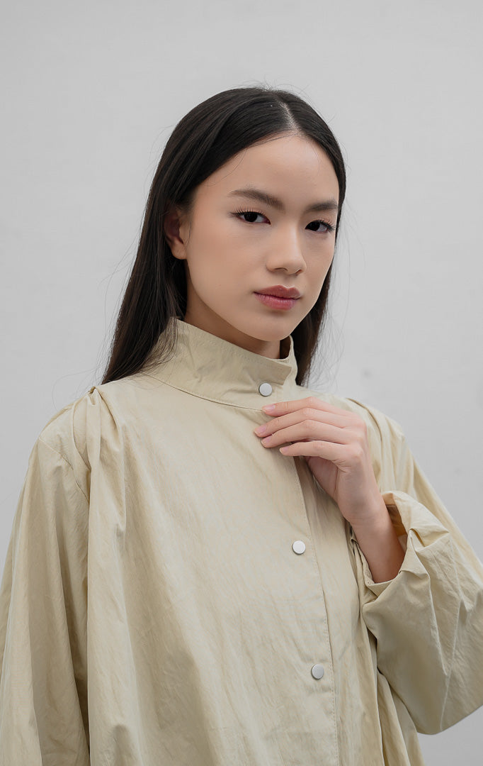 Jaket wanita warna khaki Honoria Jacket berbahan campuran crinkled cotton-nylon dengan kerah tinggi (high-neck), bukaan kancing jepret (snap-button closure), dan saku fungsional.