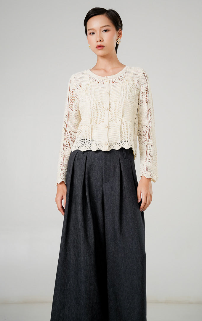 Atasan rajut kardigan wanita Inara Ivory dengan motif rajut pointelle (berlubang halus), kancing mutiara kecil di bagian depan, kerah bulat, dan lengan panjang dari This Is April. 