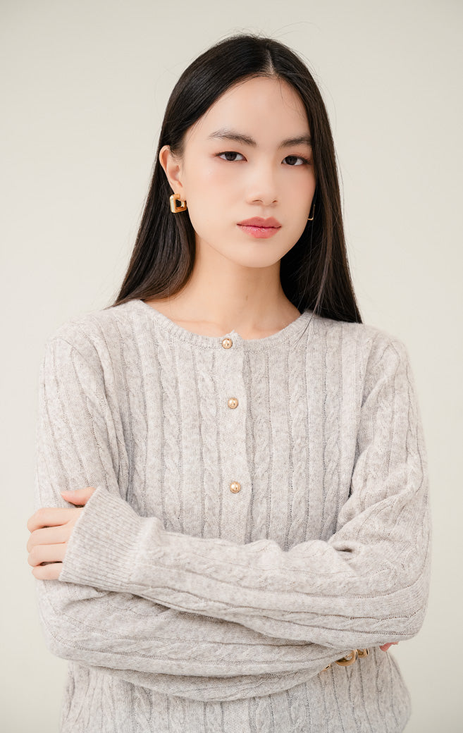 Cardigan rajut wanita Issac Cardigan warna khaki (krem/cokelat muda) motif cable knit tekstur lembut dengan aksen kancing emas (gold button) dan kerah round-neck. 