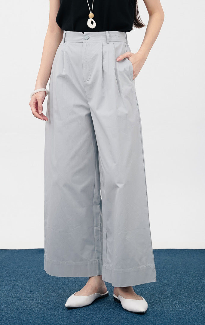 Model mengenakan Ivana Pants warna blue, celana kain wide leg dengan detail lipit depan, kancing senada, dan saku samping, dipadukan dengan sepatu flat putih.