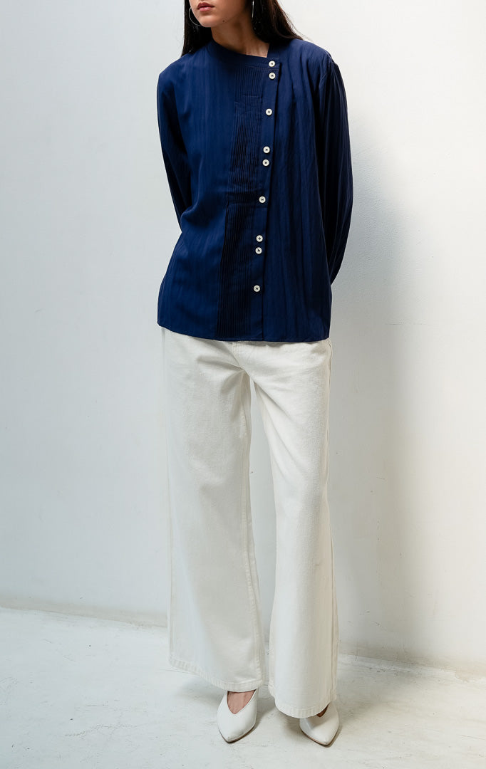 Blus wanita lengan panjang warna biru dongker (navy) Janessa Top dengan kerah asimetris (asymmetrical neckline), detail lipit pintuck vertikal di bagian depan, dan bukaan kancing tersembunyi (concealed button placket).