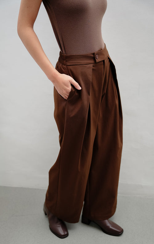 Celana panjang wanita warna cokelat tua (dark brown) Jelson Pants dengan detail lipit halus (partial pleats) di bagian depan untuk tampilan rapi dan efek kaki jenjang.