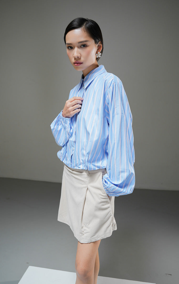 Kemeja crop wanita Jemima Top warna biru motif garis salur (striped) berbahan katun poplin dengan kerah kemeja dan detail karet bagian bawah. 