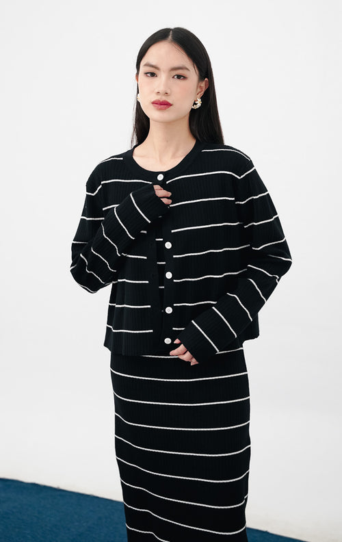 Model mengenakan Jennet Dress Set warna black, setelan yang terdiri dari gaun rajut tanpa lengan motif garis horizontal putih dan cardigan outer senada.
