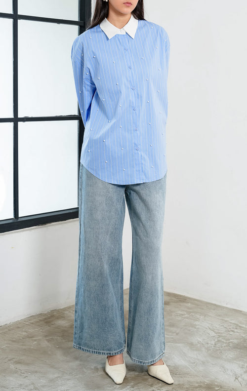 Kemeja wanita lengan panjang motif garis-garis biru (blue striped) Jeyra Top dengan aksen hiasan mutiara (pearl embellishments), kerah dan manset kontras warna putih (contrasting collar and cuffs), serta kelim melengkung (curved hem). 

