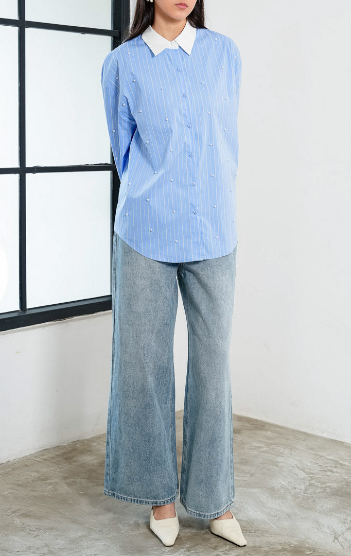 Kemeja wanita lengan panjang motif garis-garis biru (blue striped) Jeyra Top dengan aksen hiasan mutiara (pearl embellishments), kerah dan manset kontras warna putih (contrasting collar and cuffs), serta kelim melengkung (curved hem). 

