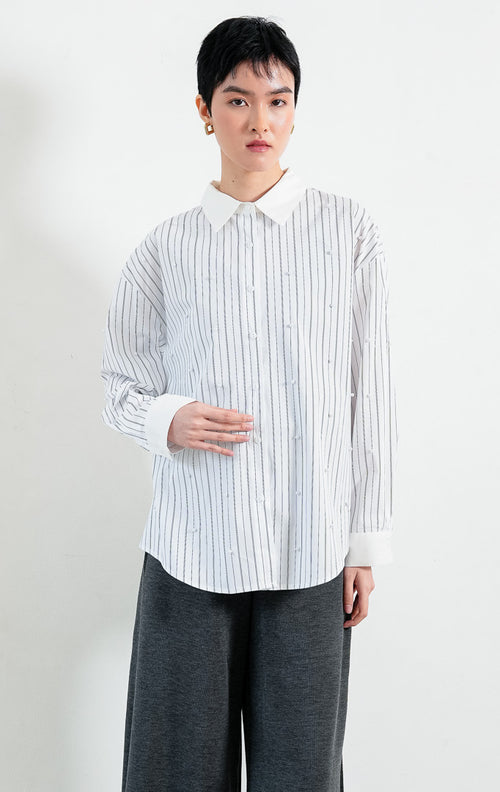 Kemeja wanita lengan panjang motif garis-garis putih (white striped) Jeyra Top dengan aksen hiasan mutiara (pearl embellishments), kerah dan manset kontras (contrasting collar and cuffs), serta kelim melengkung (curved hem). 

