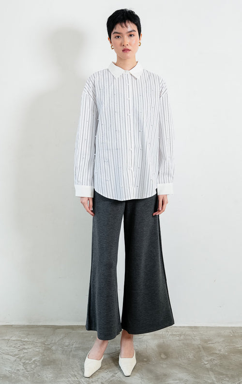 Kemeja wanita lengan panjang motif garis-garis putih (white striped) Jeyra Top dengan aksen hiasan mutiara (pearl embellishments), kerah dan manset kontras (contrasting collar and cuffs), serta kelim melengkung (curved hem). 