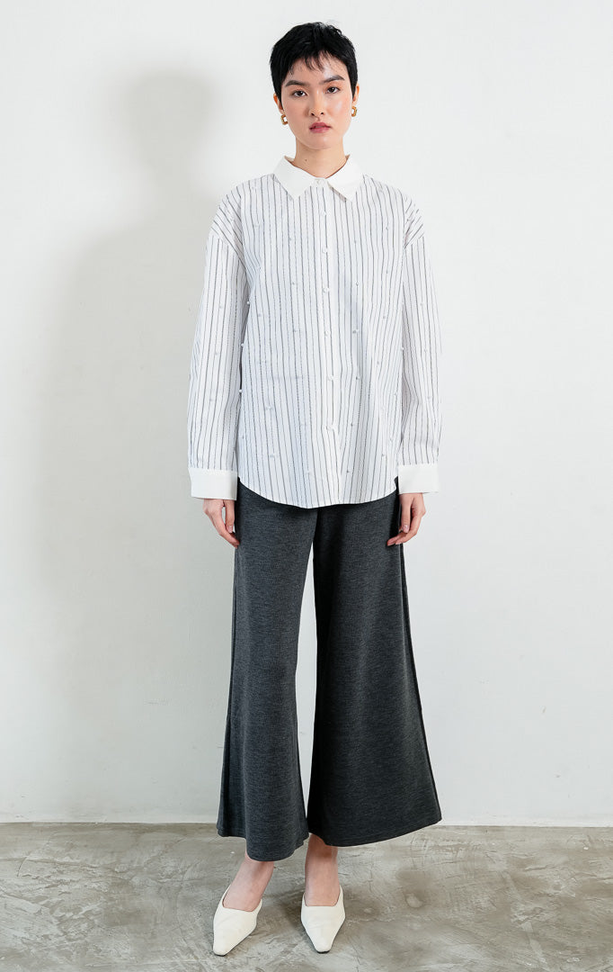 Kemeja wanita lengan panjang motif garis-garis putih (white striped) Jeyra Top dengan aksen hiasan mutiara (pearl embellishments), kerah dan manset kontras (contrasting collar and cuffs), serta kelim melengkung (curved hem). 