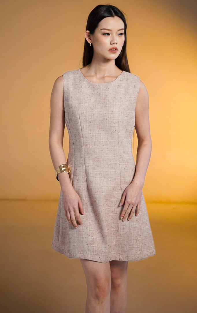 Model wanita mengenakan Jiang Mini Sleeveless A-Line Dress, gaun pendek tanpa lengan warna pink muda dengan tekstur bahan tweed berbintik, potongan A-line, dipadukan dengan gelang emas