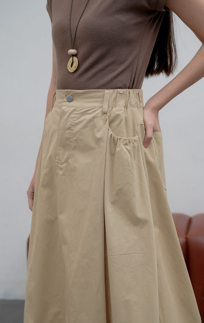 Rok balon (bubble skirt) wanita warna khaki Jinnie Skirt berbahan campuran katun-nilon terstruktur dengan siluet mekar (voluminous silhouette), detail lipitan (tucked detailing), kancing depan, dan saku samping.