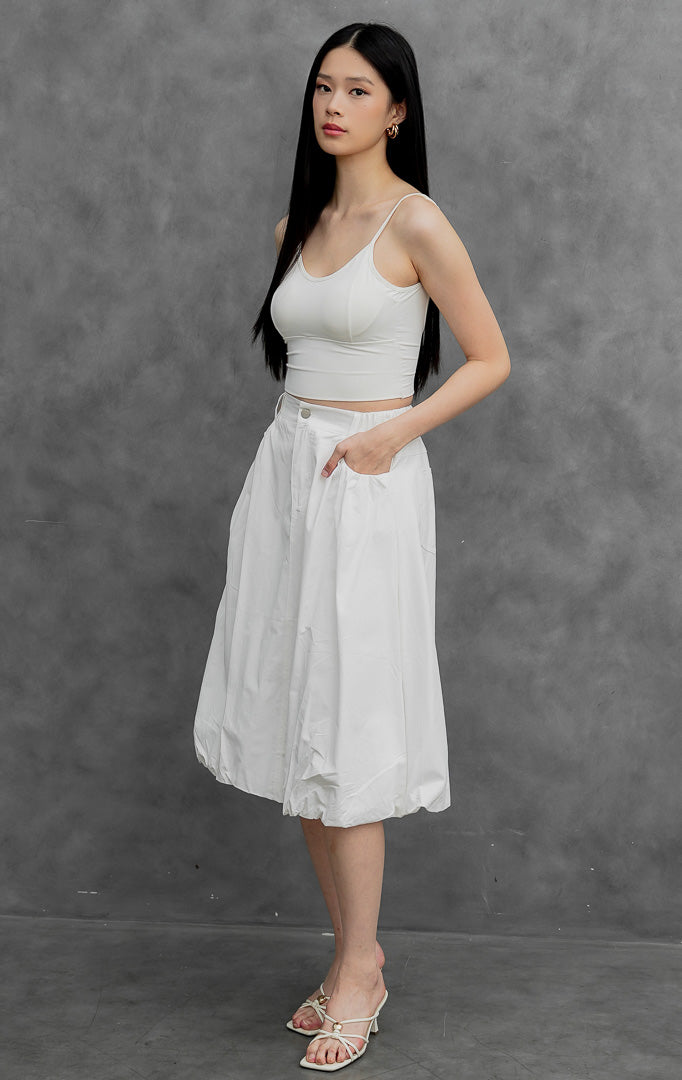 Rok balon (bubble skirt) wanita warna putih (white) Jinnie Skirt berbahan campuran katun-nilon terstruktur dengan siluet mekar (voluminous silhouette), detail lipitan (tucked detailing), kancing depan, dan saku samping.