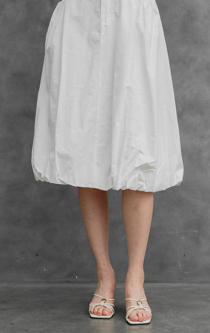 Rok balon (bubble skirt) wanita warna putih (white) Jinnie Skirt berbahan campuran katun-nilon terstruktur dengan siluet mekar (voluminous silhouette), detail lipitan (tucked detailing), kancing depan, dan saku samping.