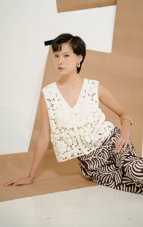 Model berpose duduk mengenakan Josephina Floral Lattice Knit Vest White, produk outerwear rompi rajut wanita tanpa lengan warna putih dengan motif bunga transparan. 