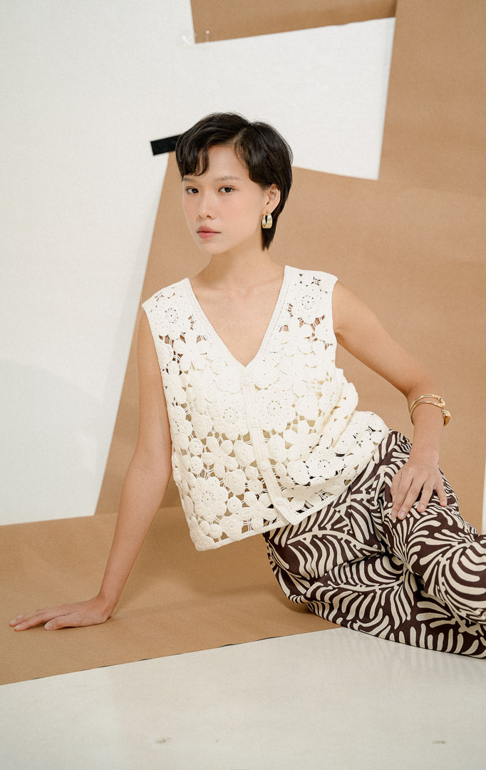 Model berpose duduk mengenakan Josephina Floral Lattice Knit Vest White, produk outerwear rompi rajut wanita tanpa lengan warna putih dengan motif bunga transparan. 