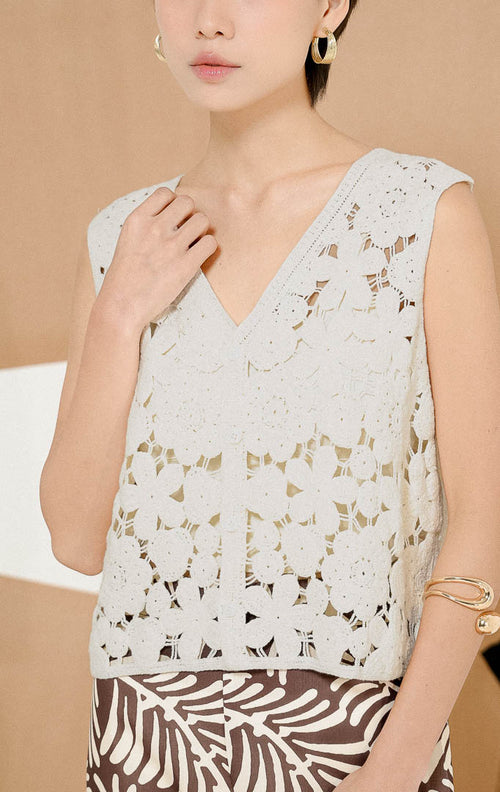Model berpose duduk mengenakan Josephina Floral Lattice Knit Vest White, produk outerwear rompi rajut wanita tanpa lengan warna putih dengan motif bunga transparan. 