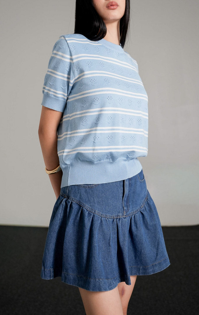 Jourdan Top, atasan rajut lengan pendek motif garis biru putih, dipadukan dengan rok mini denim biru dan sepatu hak hitam.