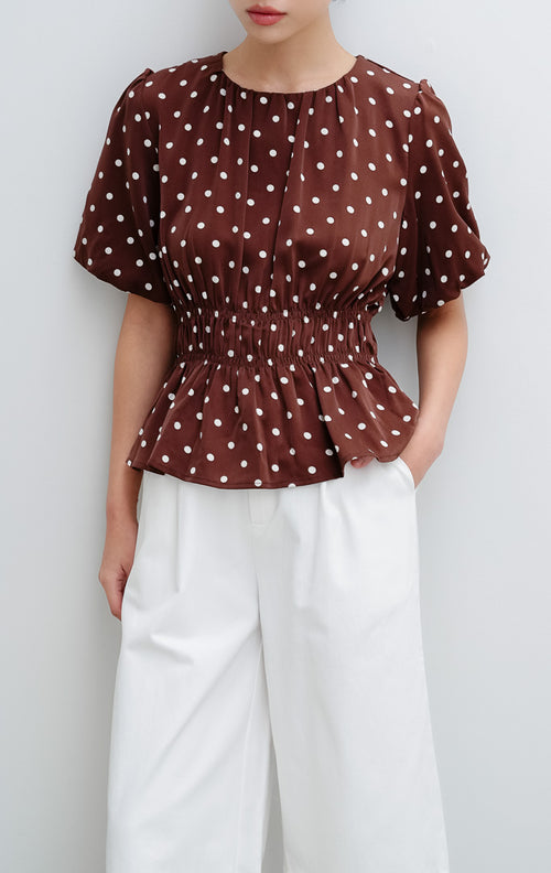 Atasan wanita warna cokelat tua (dark brown) Julietta Top bermotif polkadot dengan detail lengan balon (puff sleeves) dan badan berkerut (smocked bodice).