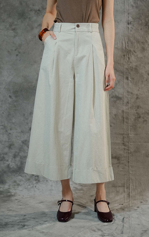 Celana kulot wanita Kahi warna ivory berbahan katun dengan siluet wide leg yang flowy, dilengkapi karet pinggang belakang dan resleting depan.