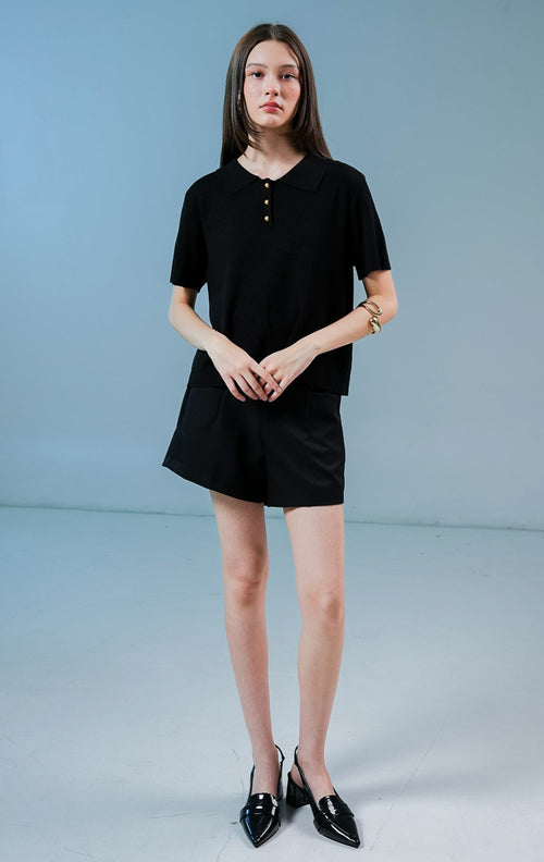 Model wanita mengenakan Griffin Collared Short Sleeve Top warna hitam, baju kaos rajut wanita lengan pendek dengan kerah terstruktur dan detail tiga kancing emas depan. 
