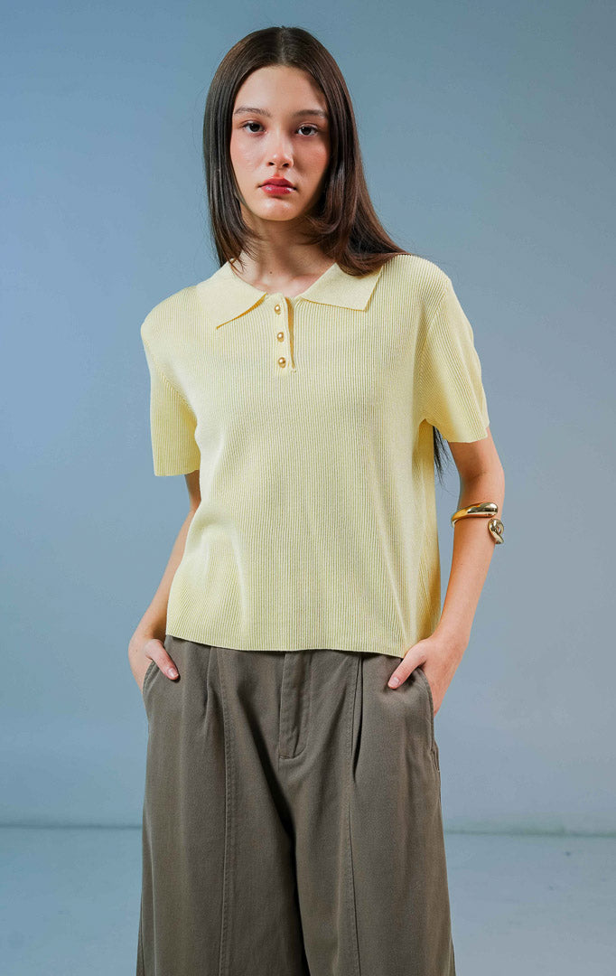 Model wanita mengenakan Griffin Collared Short Sleeve Top warna kuning muda, baju kaos rajut wanita lengan pendek dengan kerah polo terstruktur dan kancing emas depan. 