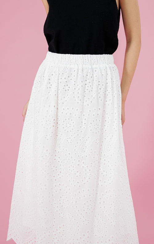 Rok putih wanita Kassidy Skirt dari This Is April dengan detail bordir eyelet seluruh bagian dan potongan pinggir bawah bergelombang (scalloped), dipadukan dengan tank top hitam.