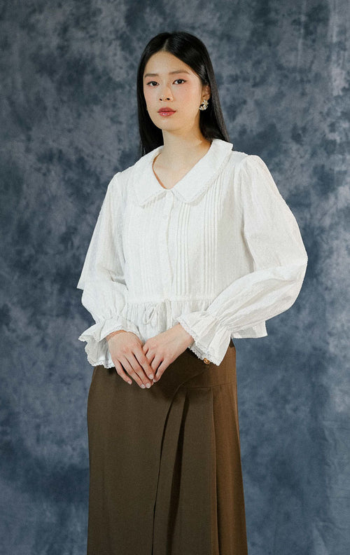 Blouse lengan panjang wanita Katherina warna putih bersih dengan kerah collar detail renda (lace), berbahan katun bertekstur, dan tali serut di pinggang.