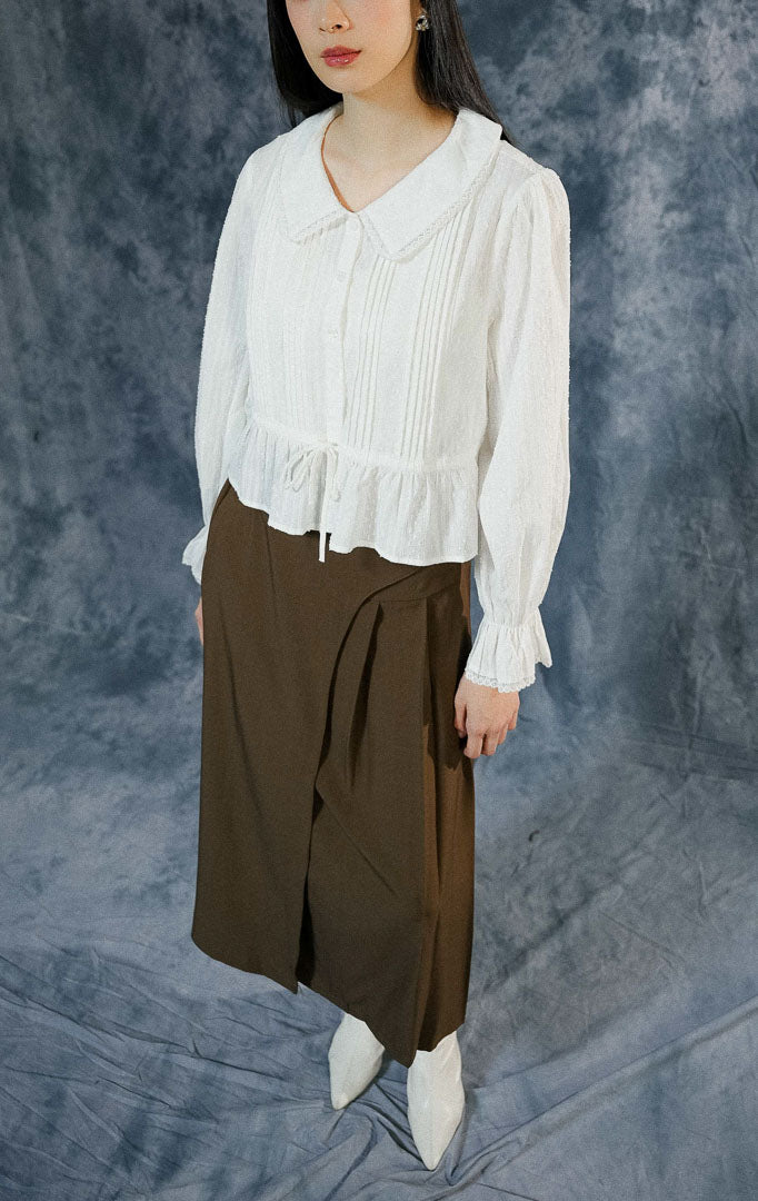 Blouse lengan panjang wanita Katherina warna putih bersih dengan kerah collar detail renda (lace), berbahan katun bertekstur, dan tali serut di pinggang.