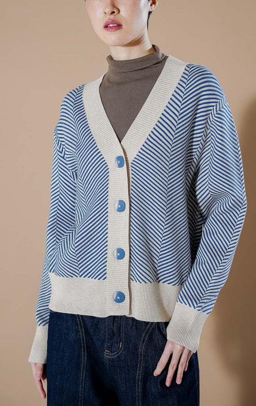 Katniss cardigan Rajut V-neck warna biru tua (dark blue) dengan motif garis diagonal, dipadukan dengan inner kerah tinggi dan celana jeans.