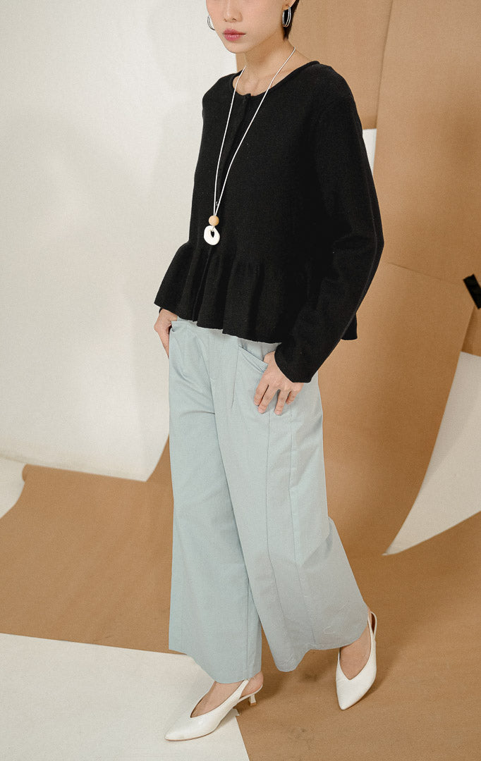 Model berdiri mengenakan Keeley Button-up Peplum Knit Cardigan Black, produk luaran cardigan rajut wanita warna hitam dengan kancing depan dan potongan peplum bergelombang. 