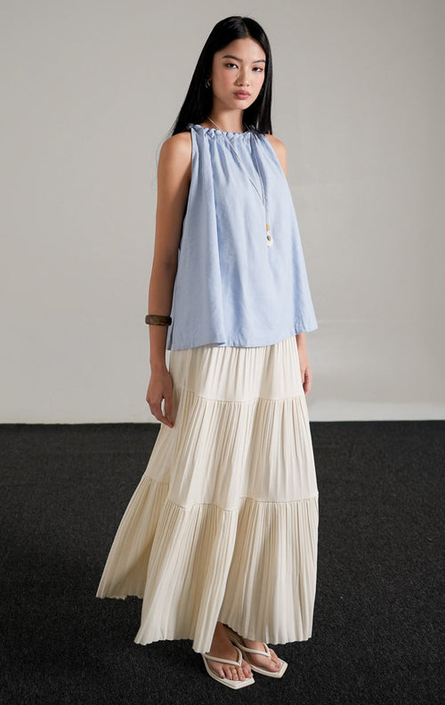Keilani Top Light Blue, atasan tanpa lengan warna biru muda dengan detail kerah kepang (braided neckline), dipadukan dengan rok panjang lipit putih.